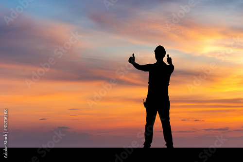 Silhouette of Factory worker man with clipping path in hard hat with thumbs up, young man celebrates with hand in the air sunset background