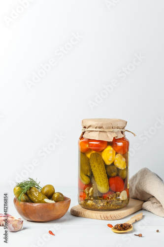 Fermented vegetables in a glass jar. Pickled cucumbers, tomatoes and squash, vertically on a light background