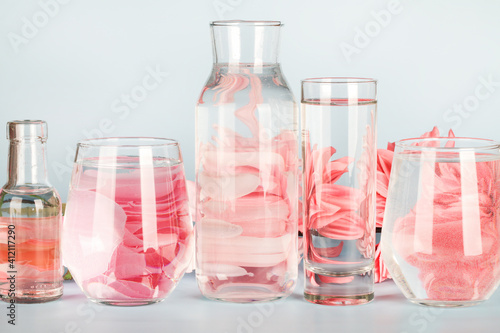 pink flowers distorted through water in glasses and bottle on blue background. Home decor, eco friendly concept.