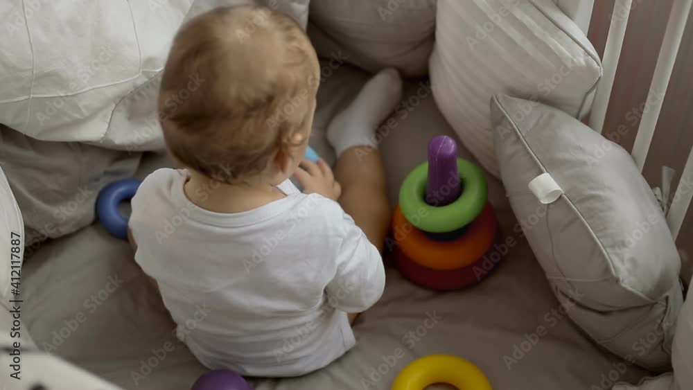 Cute baby playing with colorful rainbow toy pyramid sitting in bed. Cute baby playing with colorful rainbow toy pyramid sitting in bed.