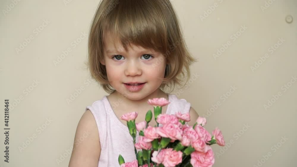 Portrait of little 2 year old child girl holds bouquet of flowers, pink carnations, looks at camera, smiles and smells flowers. Spring and holiday concept Portrait of little 2 year old child girl holds bouquet of flowers, pink carnations, looks at camera, smiles and smells flowers. Spring and holiday concept