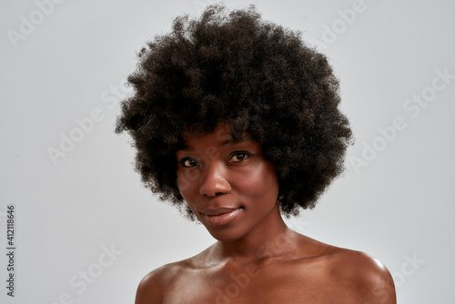 Beauty portrait of attractive african american young woman with afro hair and perfect smooth glowing skin looking at camera while posing isolated over gray background