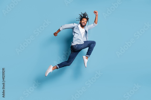 Full length profile portrait of carefree dark skin guy rush speed toothy smile isolated on blue color background © deagreez