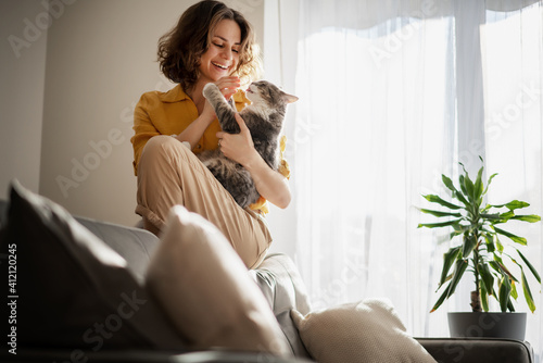 Beautiful cheerful young woman with a cute gray cat in her arms at home in the interior, friendship and love for pets photo