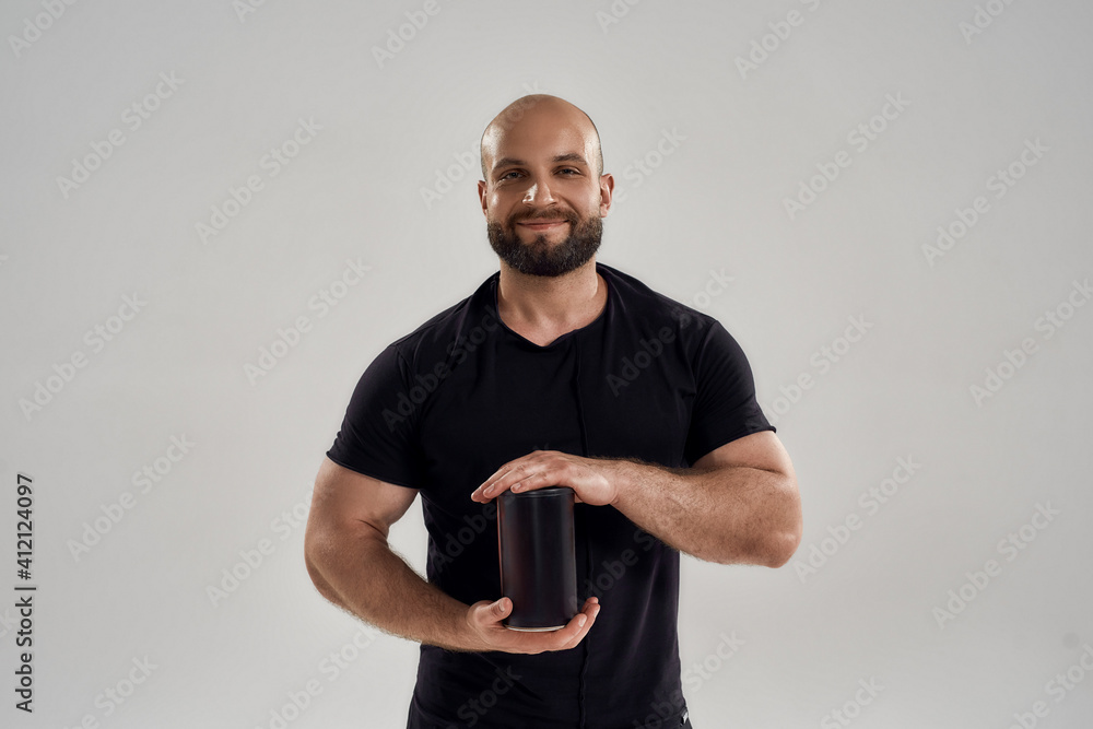 Smiling young muscular caucasian man showing protein bottle Smiling young muscular caucasian man showing protein bottle