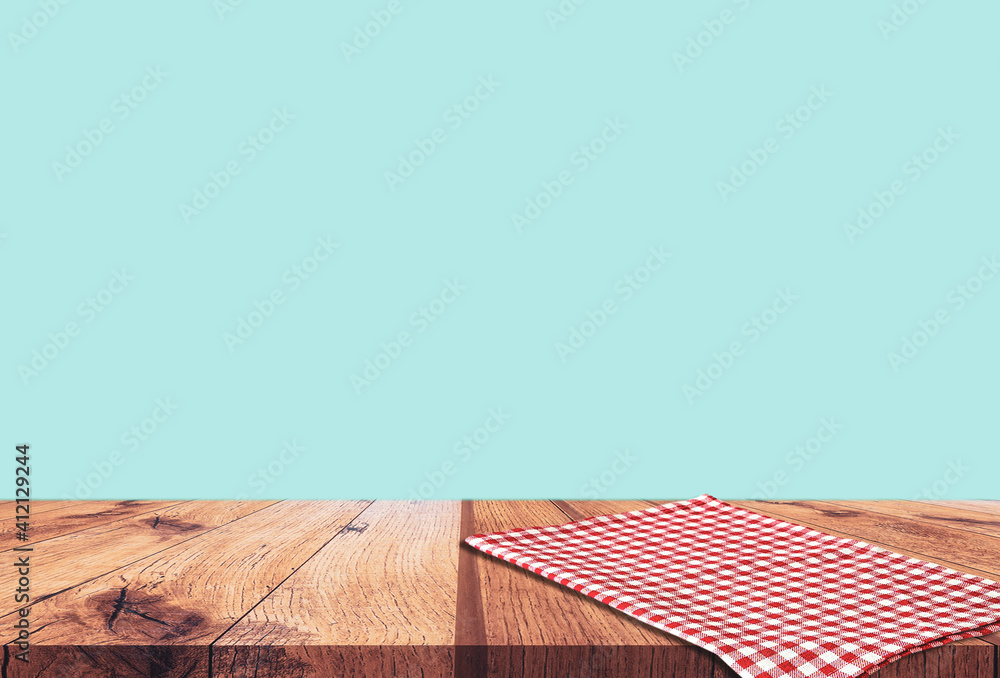 Empty wooden table with red checked tablecloth over blue wall background