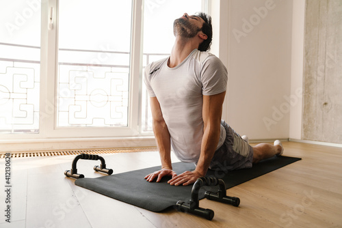 Obraz na plátně Focused athletic man stretching his body while working out at home