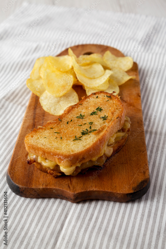 Homemade French Onion Melt Cheese Sandwich with Chips on a rustic wooden board on cloth, side view. Homemade French Onion Melt Cheese Sandwich with Chips on a rustic wooden board on cloth, side view.