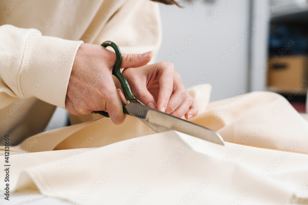 Caucasian nice girl seamstress cutting fabric while working in atelier
