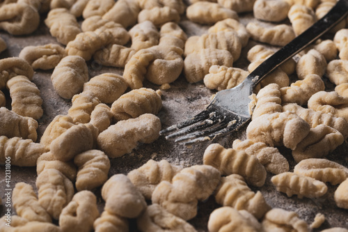 floured fork holding a gnocchi, background with many gnocchi, homemade food