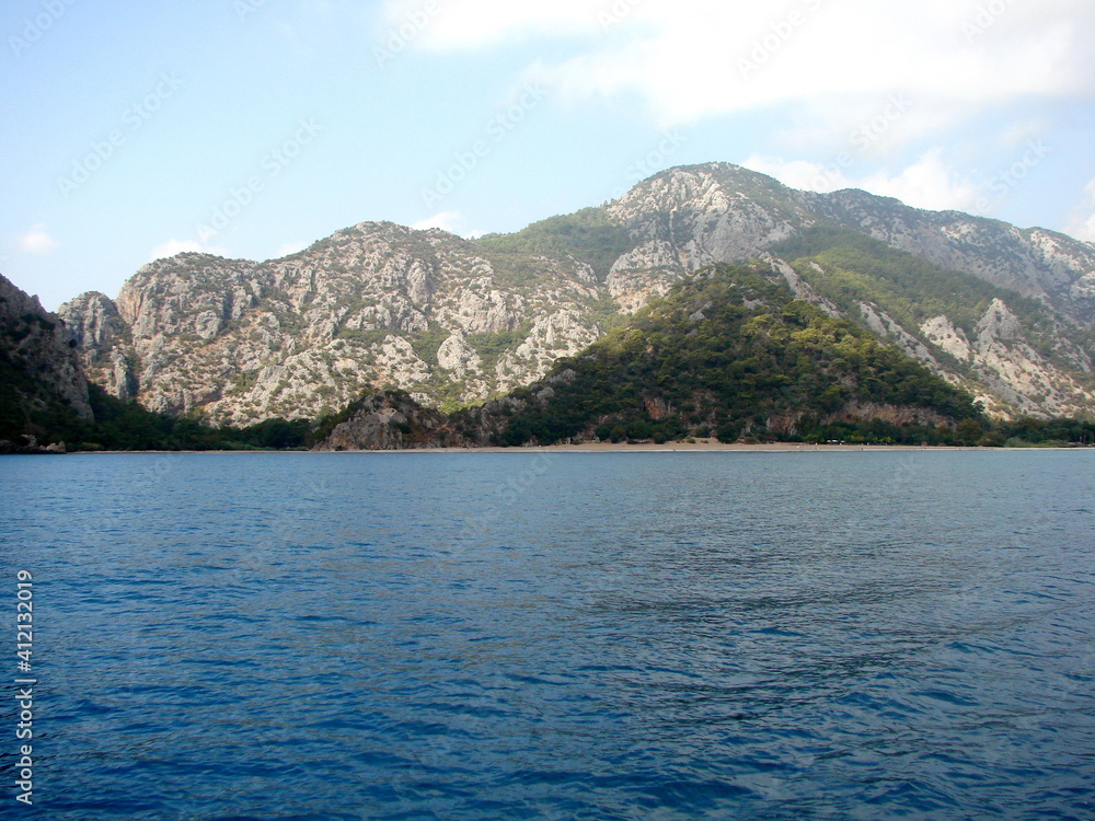 Panorama of the blue sea surface on the background of mountain ranges illuminated by the morning sun on the horizon.