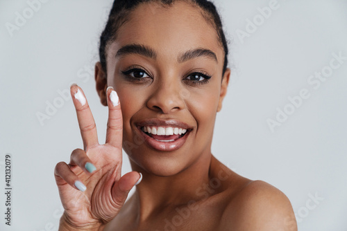 Joyful shirtless african american woman showing face cream