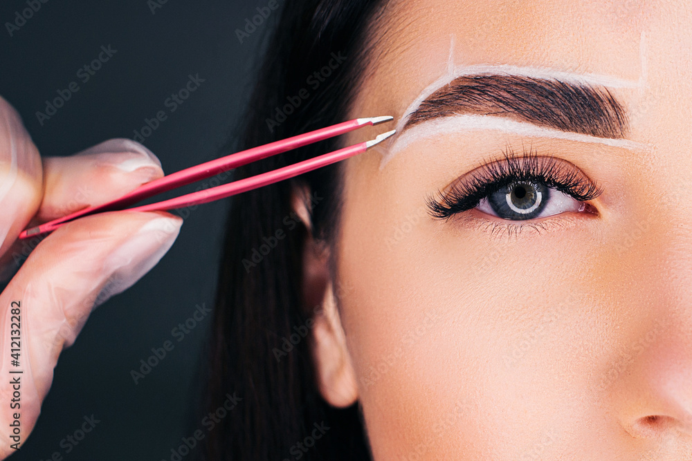 Fototapeta premium We make eyebrows with pink tweezers, close-up background for the eyebrow.