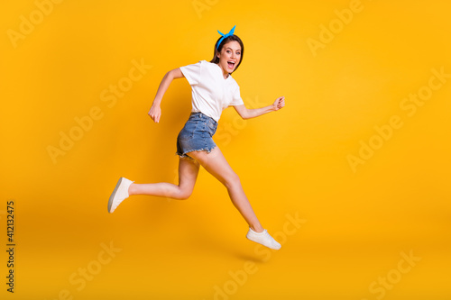 Full length body size side profile photo of female runner laughing jumping high isolated on vivid yellow color background
