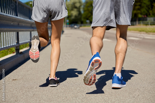 fitness, sport and healthy lifestyle concept - feet of sporty couple running along city road