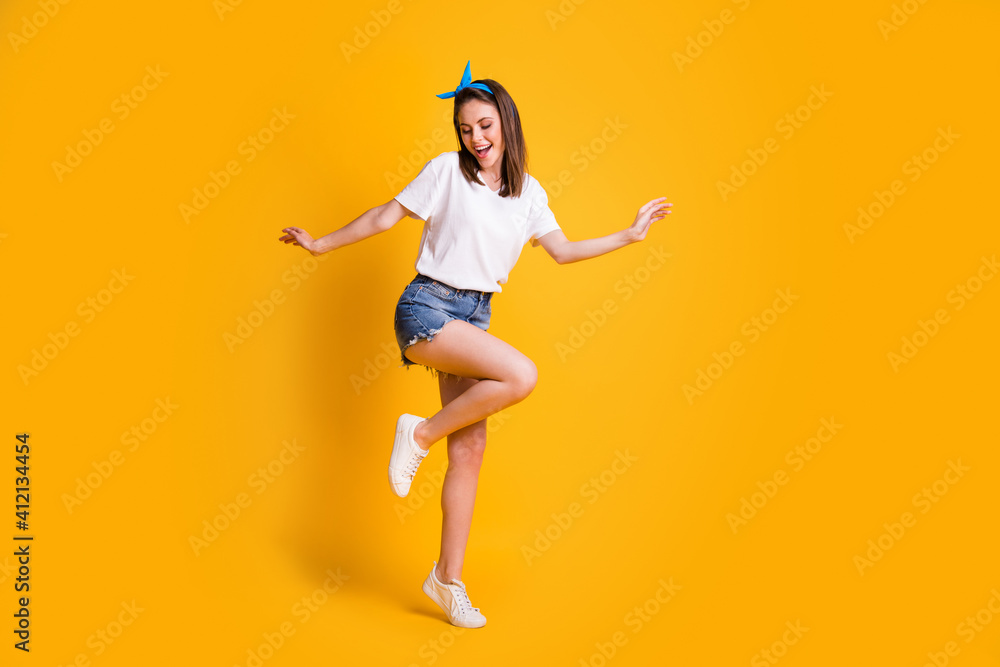 Full length body size view of fit cheerful brown-haired girl jumping dancing enjoying free time isolated over bright yellow color background Full length body size view of fit cheerful brown-haired girl jumping dancing enjoying free time isolated over bright yellow color background