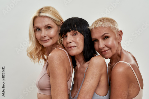 Close up portrait of three beautiful happy mature women in underwear posing together isolated over light background