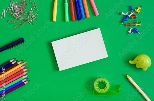 Stationery for drawing and school, note paper, pen, markers, pencils, paper clips, push pins, tape and pencil sharpener on a green background