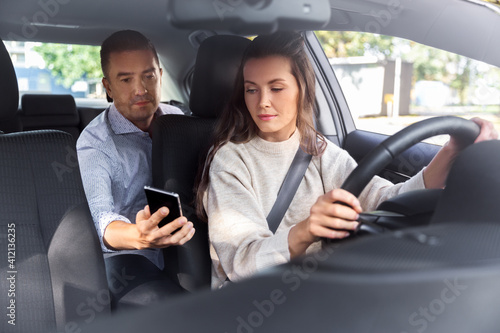 transportation  vehicle and people concept - male passenger showing smartphone to female taxi car driver