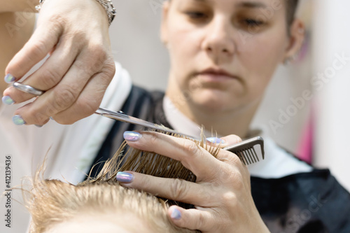 Close-up of hairdresser cutting boy's hair with scissors.