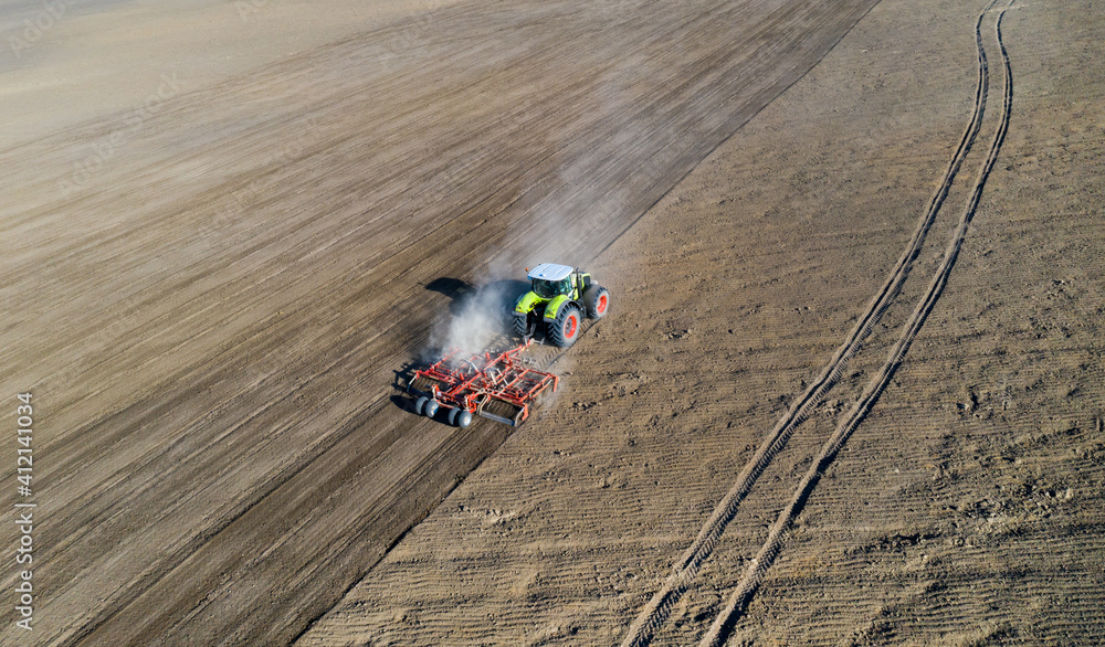 A farmer in a tractor prepares land with a sowing cultivator as part of pre-sowing work at the beginning of the spring agricultural season on agricultural land.