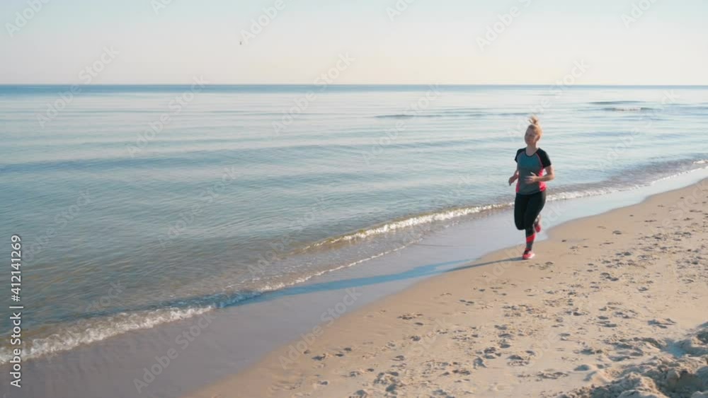 Woman and running exercising healthy active lifestyle jogging along the surf line of the sea beach in summer. Happy sports girl outside. Stabilizer shot in slow motion. Woman and running exercising healthy active lifestyle jogging along the surf line of the sea beach in summer. Happy sports girl outside. Stabilizer shot in slow motion.