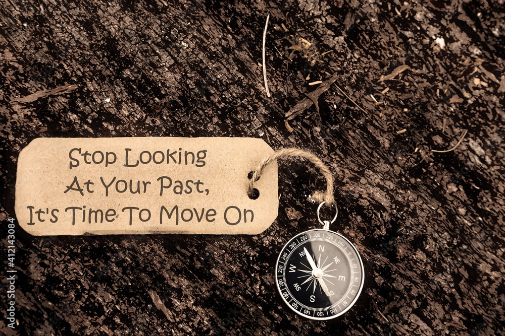 Fototapeta premium Conceptual Image: Magnetic compass with paper tag written Stop Looking At Your Past, It's Time To Move On, selective focus.
