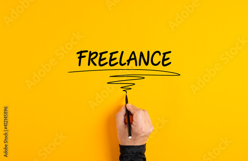 Male hand writing freelance on yellow background. Freelance job or working as a freelancer concept.. photo