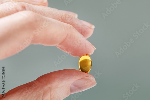 Female hand holding a small yellow capsule of nutritional supplement. Food supplement, vitamin D, omega, vitamin C, multivitamins. Soft focus