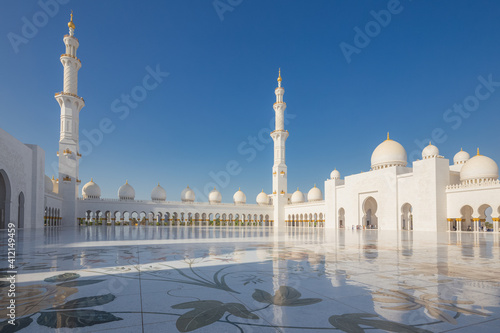 An empty courtyard with and exterior view of the Sheikh Zayed Grand Mosque on a clear sunny day in Abu Dhabi, UAE.