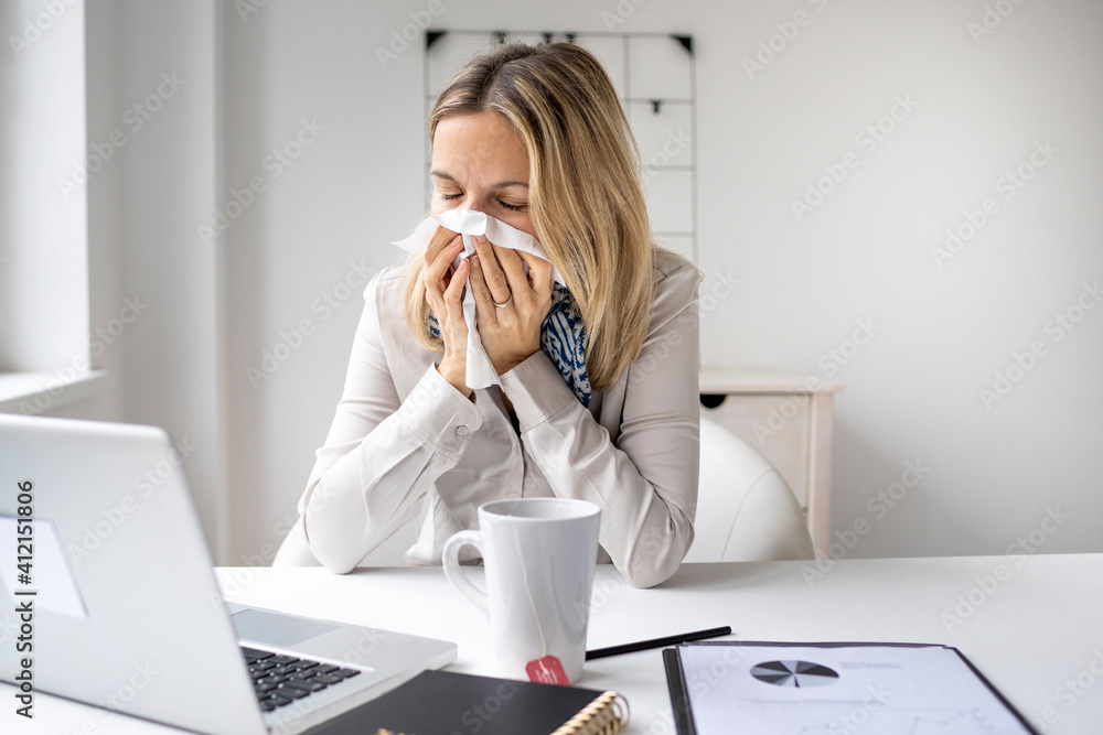 Business woman in office feeling unwell sitting in front of her laptop blowing her nose, stressed femal employee have anxiety attack at workplace Business woman in office feeling unwell sitting in front of her laptop blowing her nose, stressed femal employee have anxiety attack at workplace