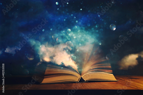 Magical image of open antique book over wooden table with glitter overlay photo