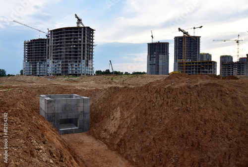 Construction of stormwater pits, sanitary sewer system distribution chamber and pump station. Sewerage manhole and pipes. Tower cranes in action at construction site. Excavator on earthworks