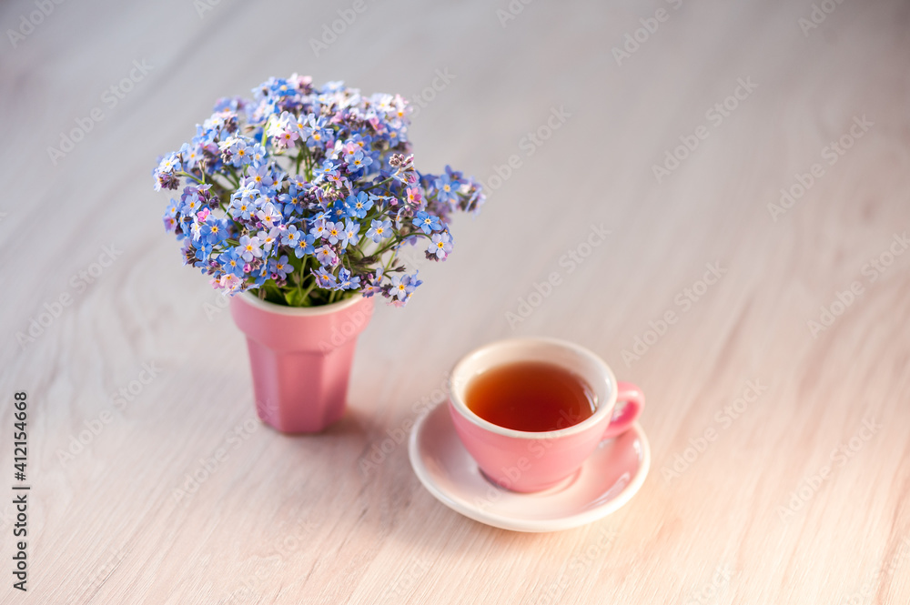 A bouquet of forget-me-not flowers on a table with a cup of tea. Holiday background, copy space, soft focus. Mothers day, birthday concept.