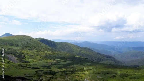 aerial view of green mountains with trees and valleys on a background of blue sky
