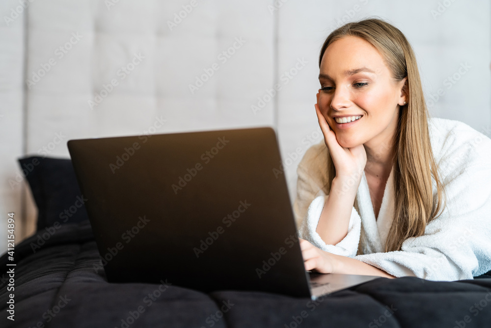 Young woman in bedrobe working on computer in bed Young woman in bedrobe working on computer in bed