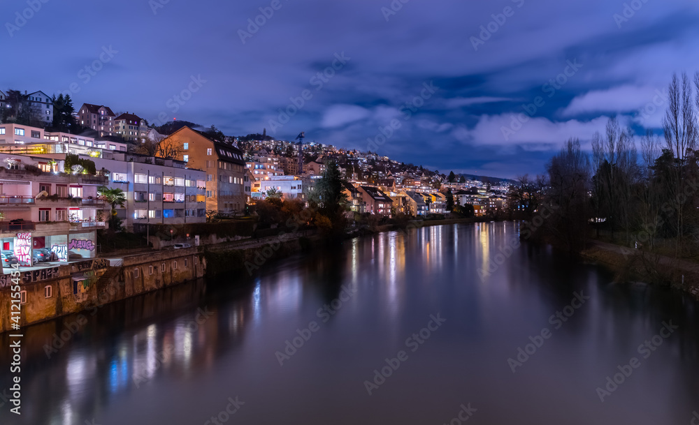 Blue hour in Zürich, the largest city in Switzerland. Illuminated houses along the Limmat River and their reflections in the water