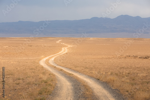 An empty dusty desert dirt road zig zags out to a distant horizon in Charyn Canyon National Park in the Almaty Province of Kazakhstan.