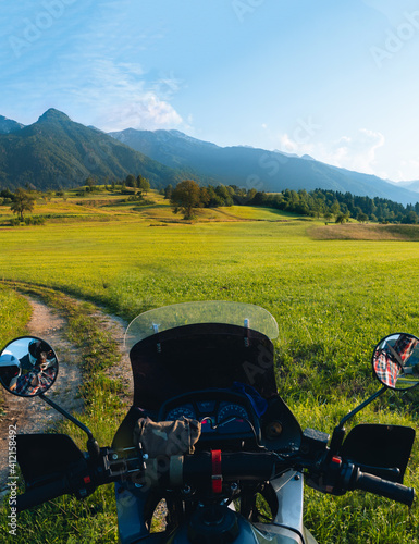 First person View tourer motorcycle steering wheel on dirt road. beautiful green field. World adventure rider. Tourist bike. Slovenia mountains, expedition. discovery. summer day. Vertical photo