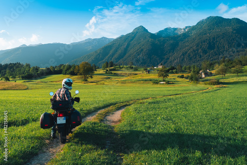 Man motorcyclist ride touring motorcycle. Alpine mountains on background. Biker lifestyle, world traveler. Summer sunny sunset day. Green hills. hermetic packaging bags. copy space. Slovenia