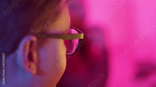 View from the back of a young man who looks at the monitor. Pink bright light. Dark in the room, night. 4k video.