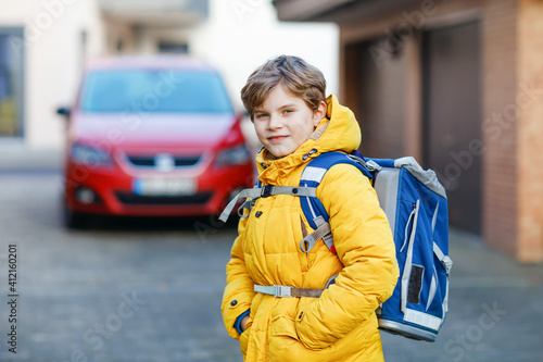 Little school kid boy of elementary class walking to school. Portrait of happy child on the street with traffic. Student with in yellow jacket and backpack in colorful winter clothes. photo