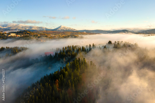 Aerial view of a small distant village houses on hill top in fall foggy mountains at sunrise.