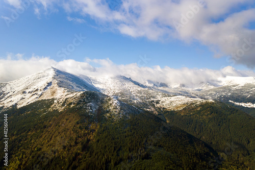 High mountain peaks covered with autumn spruce forest and high snowy summits.