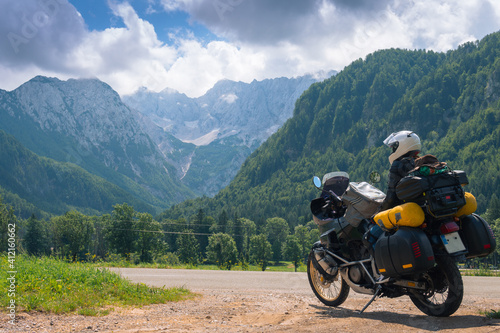 Girl in full body protection, turtle armor, knee pads and helmet, tourer motorcycle for traveling with large luggage, on a background of green mountains, travel and freedom. Zgornje Jezersko Slovenia