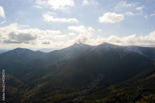 Aerial view of majestic mountains covered with green spruce forest and high snowy peaks. © bilanol
