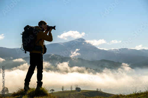 Dark silhouette of a hiker photographer taking picture of morning landscape in autumn mountains.