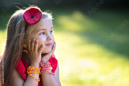 Portrait of pretty fashionable child girl in red dress enjoying warm sunny summer day.