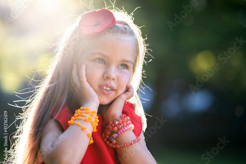 Portrait of happy pretty child girl in red dress smiling outdoors enjoying warm sunny summer day.