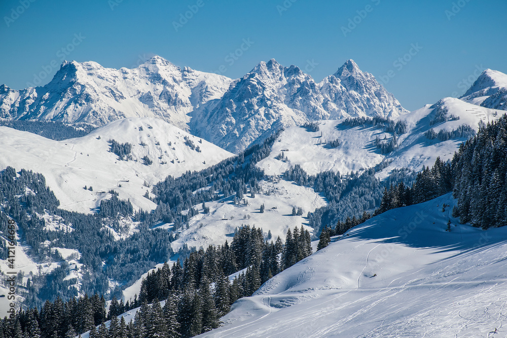The Austrian Alps in winter near Kitzbuhel. Behind the snow covered fir trees the fog rises revealing the magnificent mountain peaks.